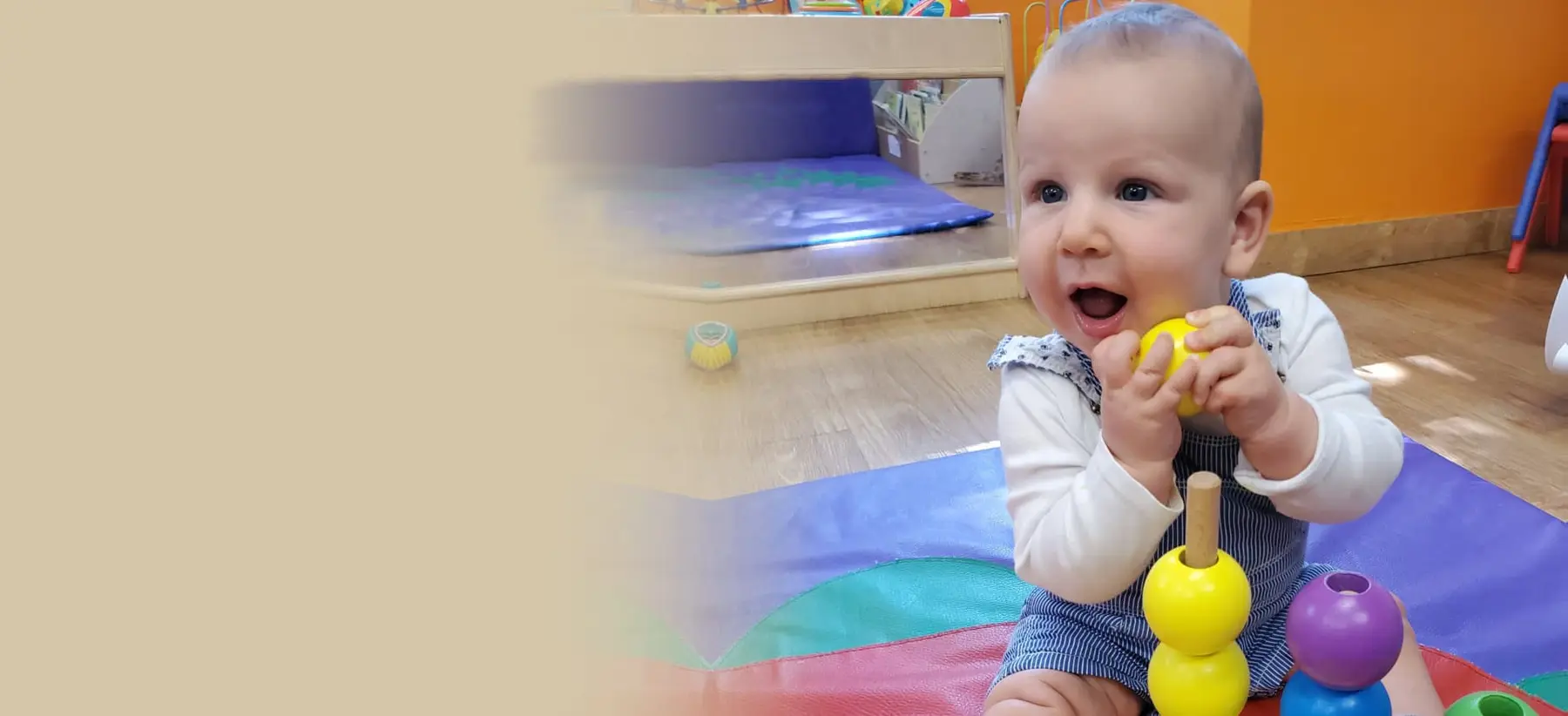 A baby sitting on a colorful mat holds a yellow toy piece while looking up with an open mouth.
