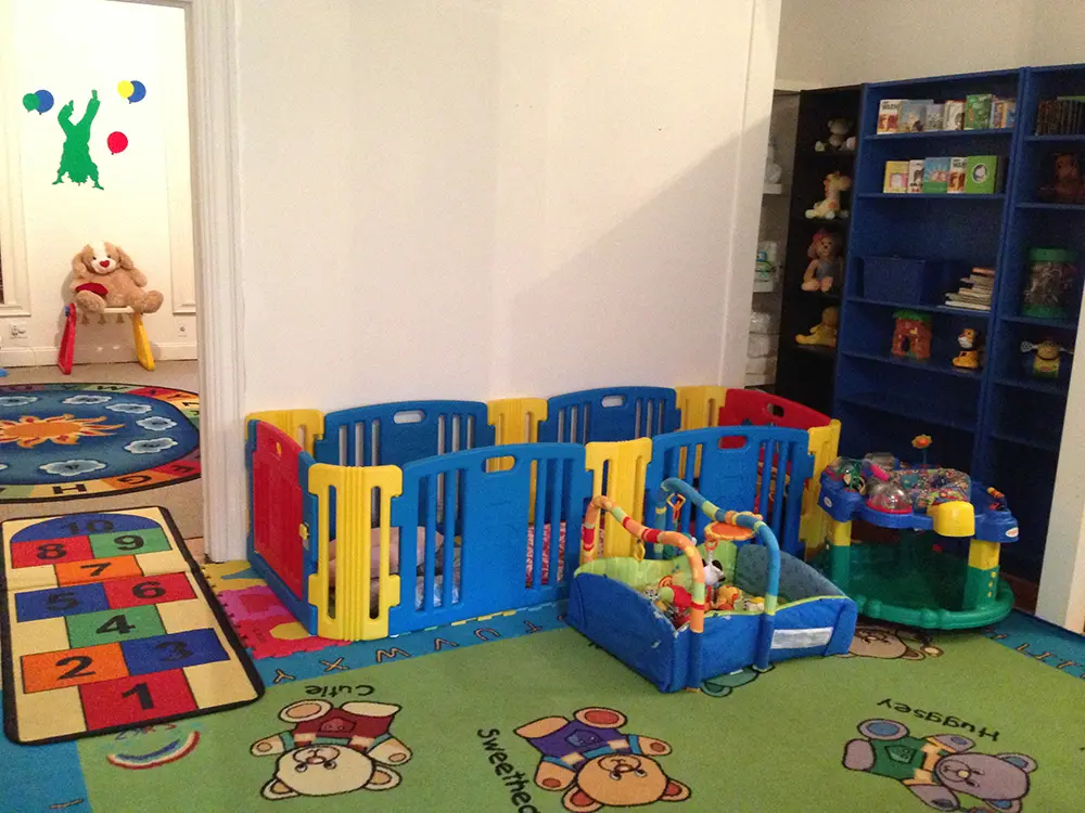 A playroom with colorful toys, a baby gate, and educational rugs on the floor.