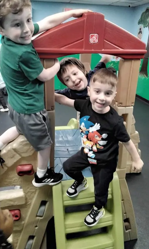Three young boys interacting on a colorful indoor play structure with green and red plastic components.