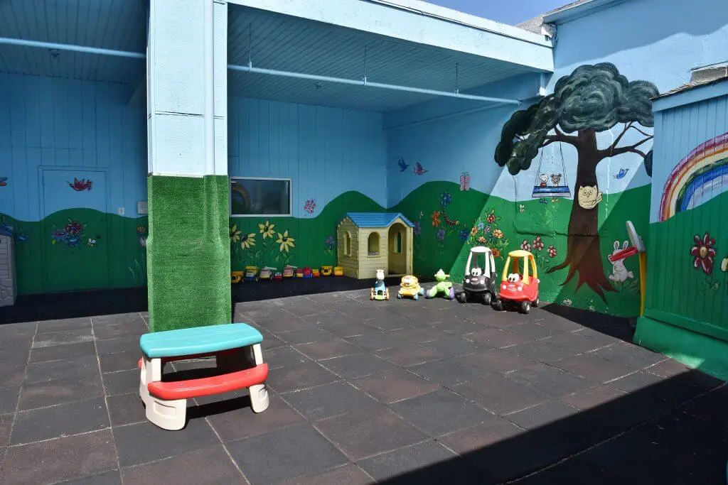Outdoor play area with toy cars, a small house, and painted murals on blue walls.
