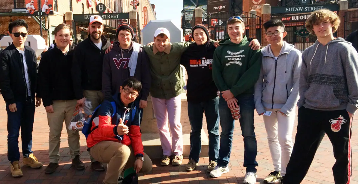 A group of ten people, including one kneeling in front, pose together on a brick plaza with street signs and buildings behind them.