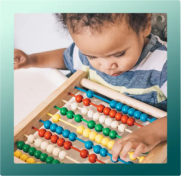 A young boy looks down while playing with a colorful wooden abacus on a table.