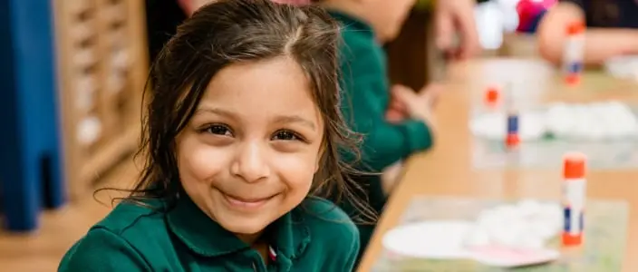 A smiling girl in a green shirt sits at a table with craft supplies and paper plates.