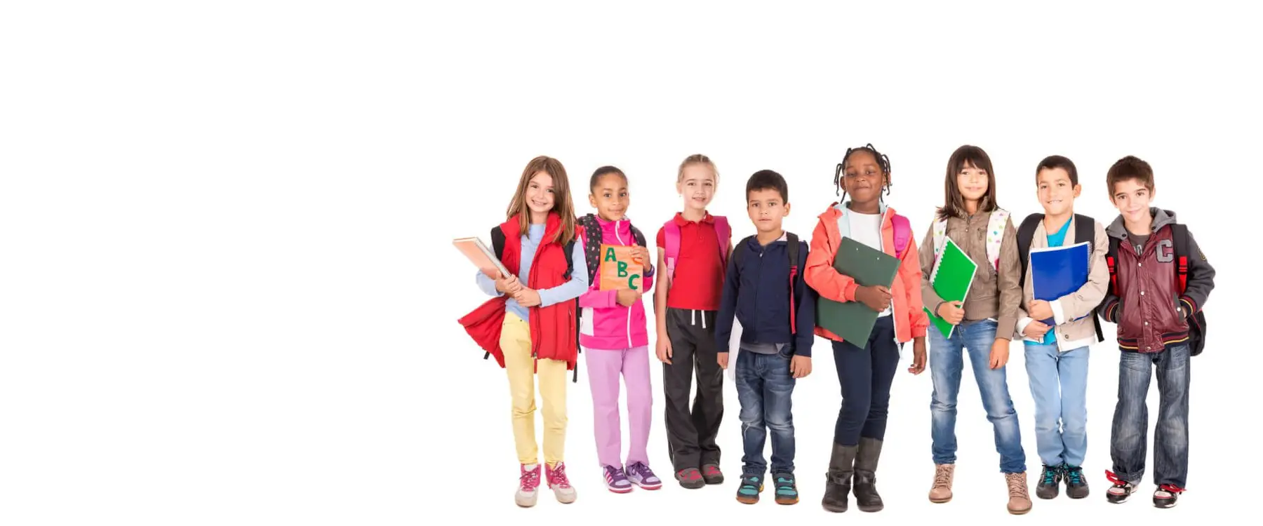 Eight children stand in a row against a white background, holding books, folders, and backpacks while facing forward.