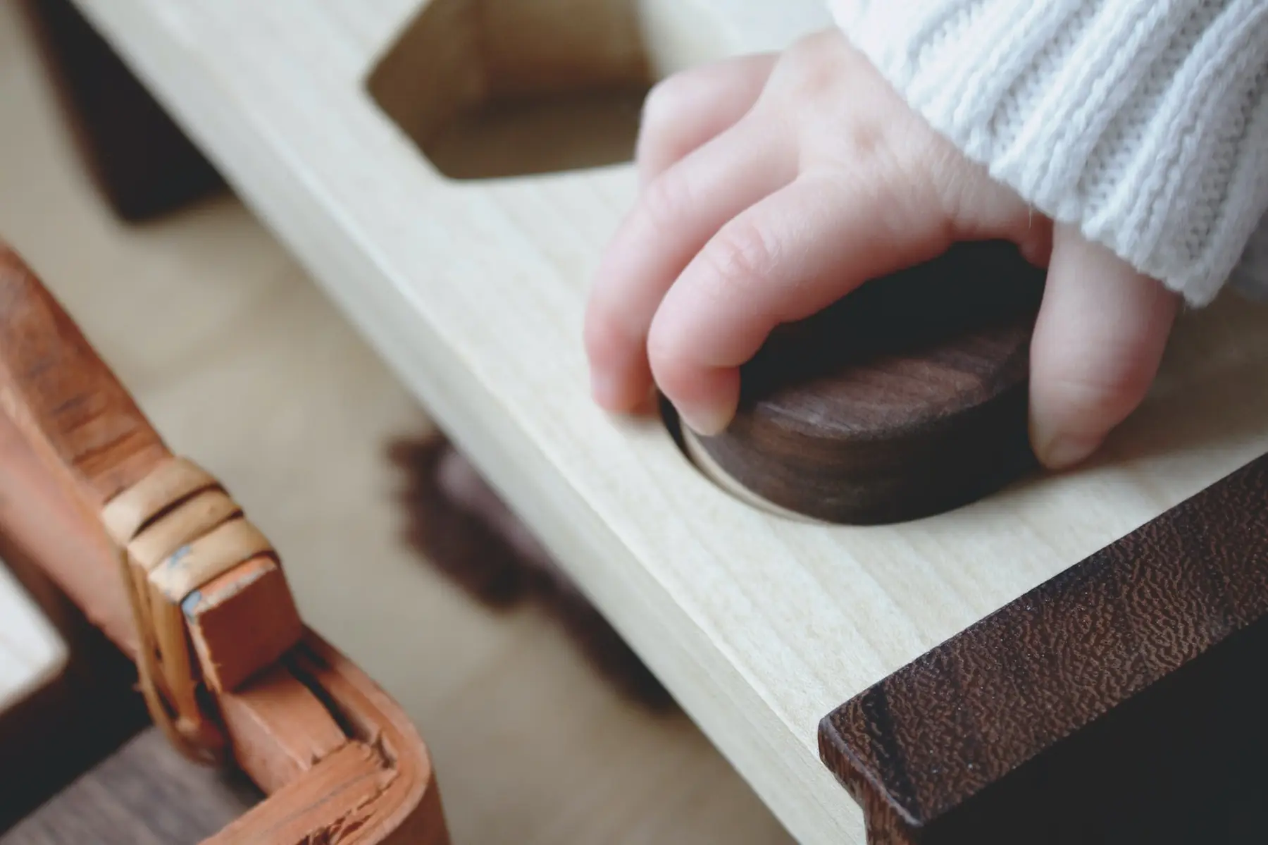 A child's hand wearing a white knit sleeve rests on a dark wooden knob attached to a light-colored wooden structure.