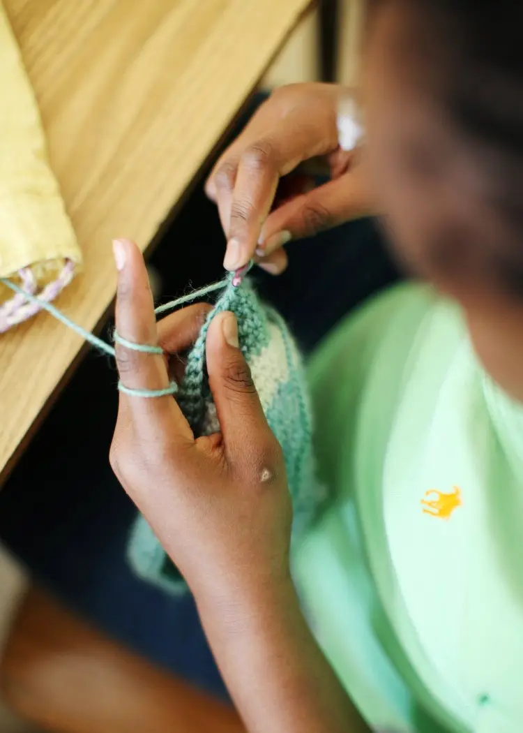 A person's hands hold knitting needles and green yarn while working on a knitted piece.