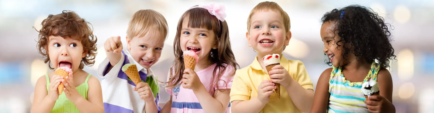 Five young children hold and eat ice cream cones while looking in different directions against a blurred background.