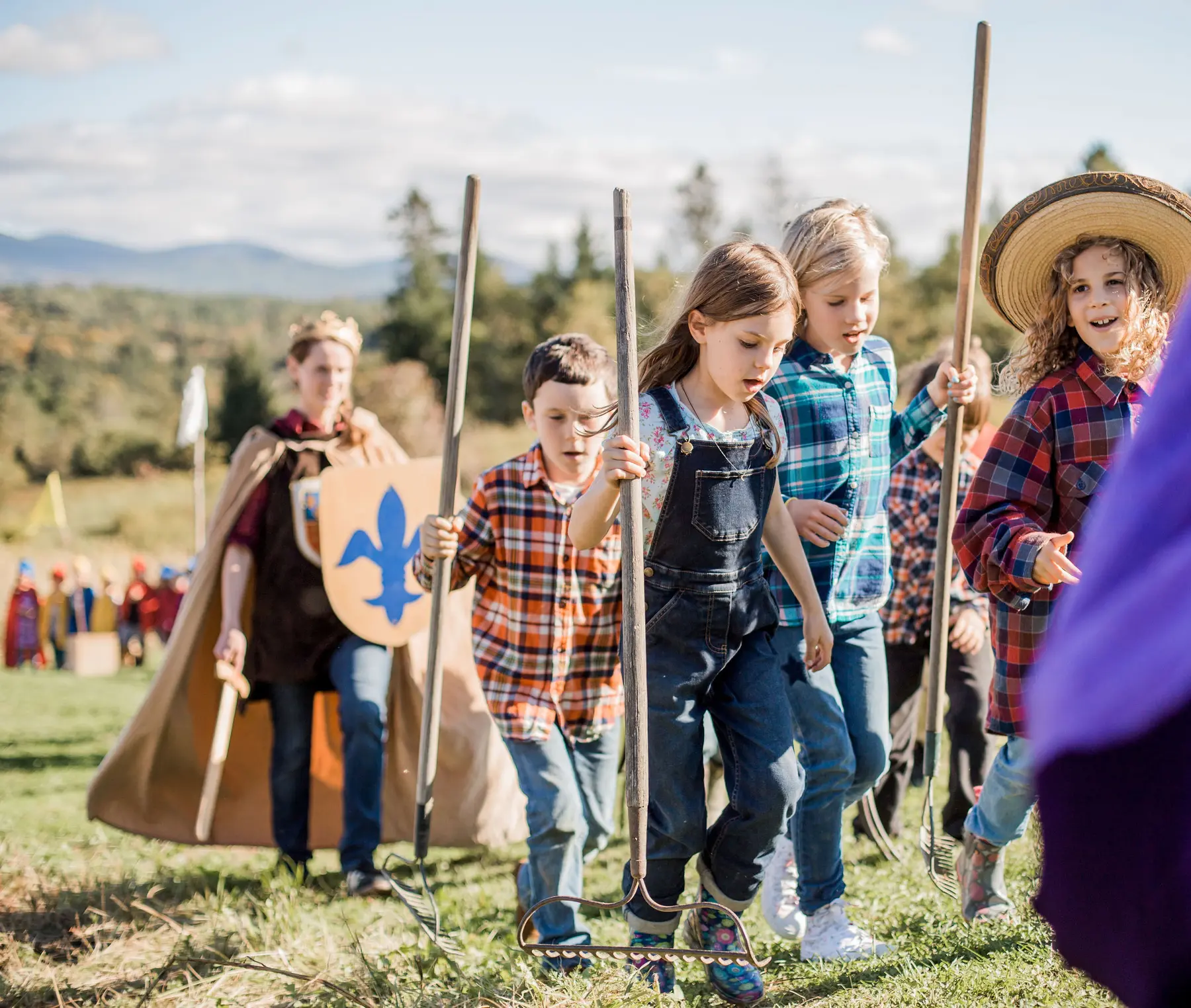 Children in plaid shirts and overalls carry long-handled rakes and a hoe across a grassy field while a woman in a cape and crown holds a shield behind them.