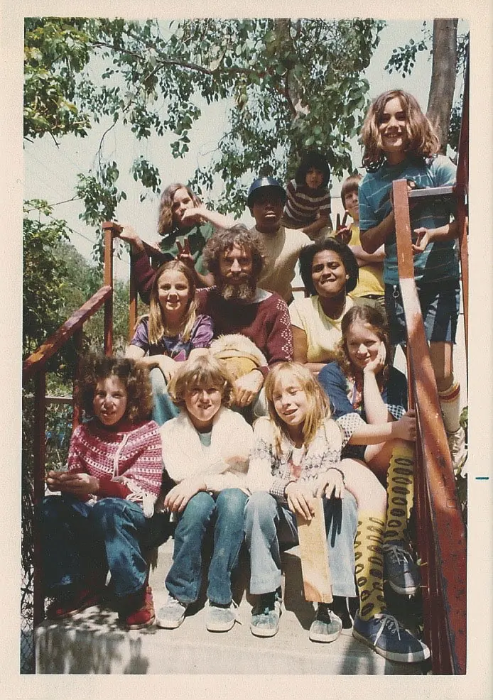 A group of twelve people of various ages sit and stand on outdoor wooden stairs, with some smiling at the camera and one person holding up a peace sign.