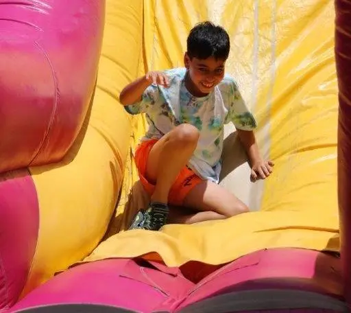 A boy sits on a yellow inflatable slide with pink side walls, smiling and looking toward the camera.