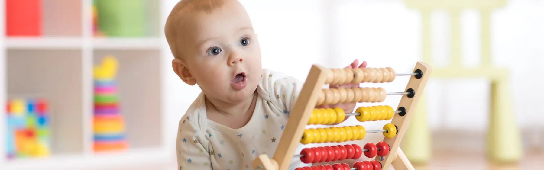 A baby sitting at a table with an open mouth while touching a wooden abacus toy with colorful beads.