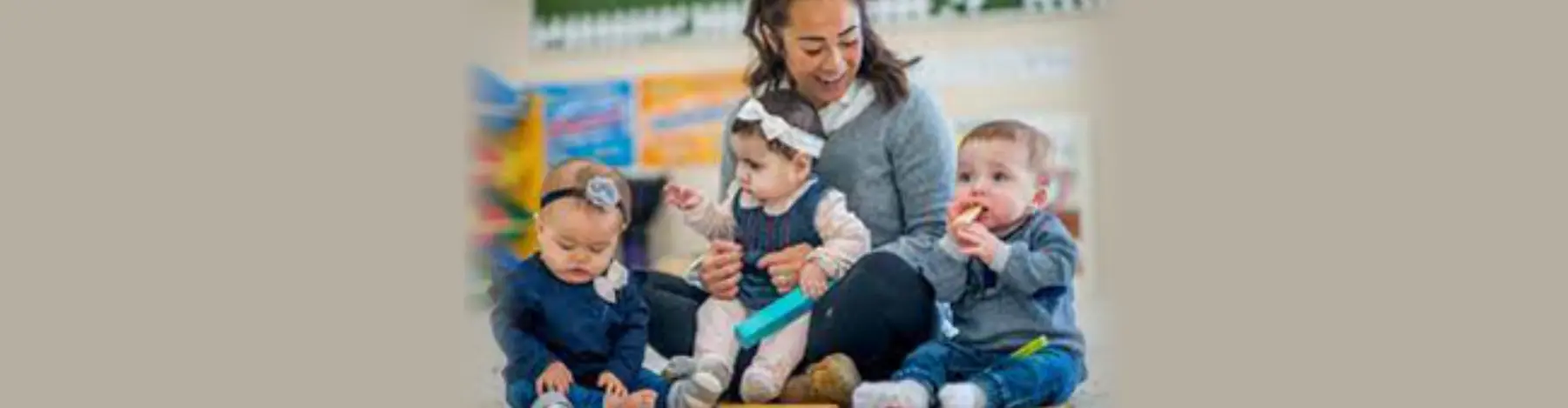 A woman sits on the floor with three babies, holding one while another holds a blue toy and a third holds an object near his mouth.