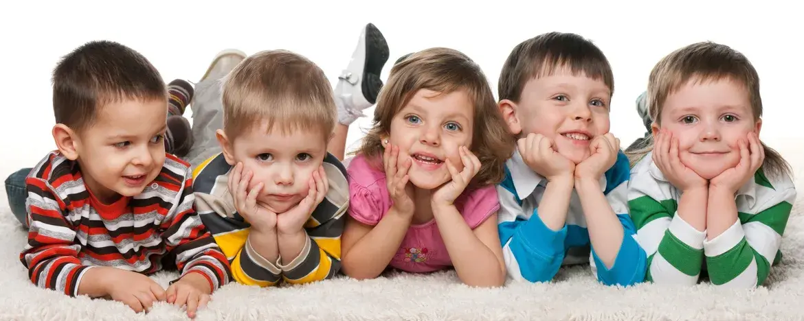 Five young children lying on a white carpet with hands near faces