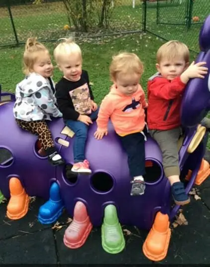 Four toddlers sitting on a purple playground structure with colorful boot-shaped supports.