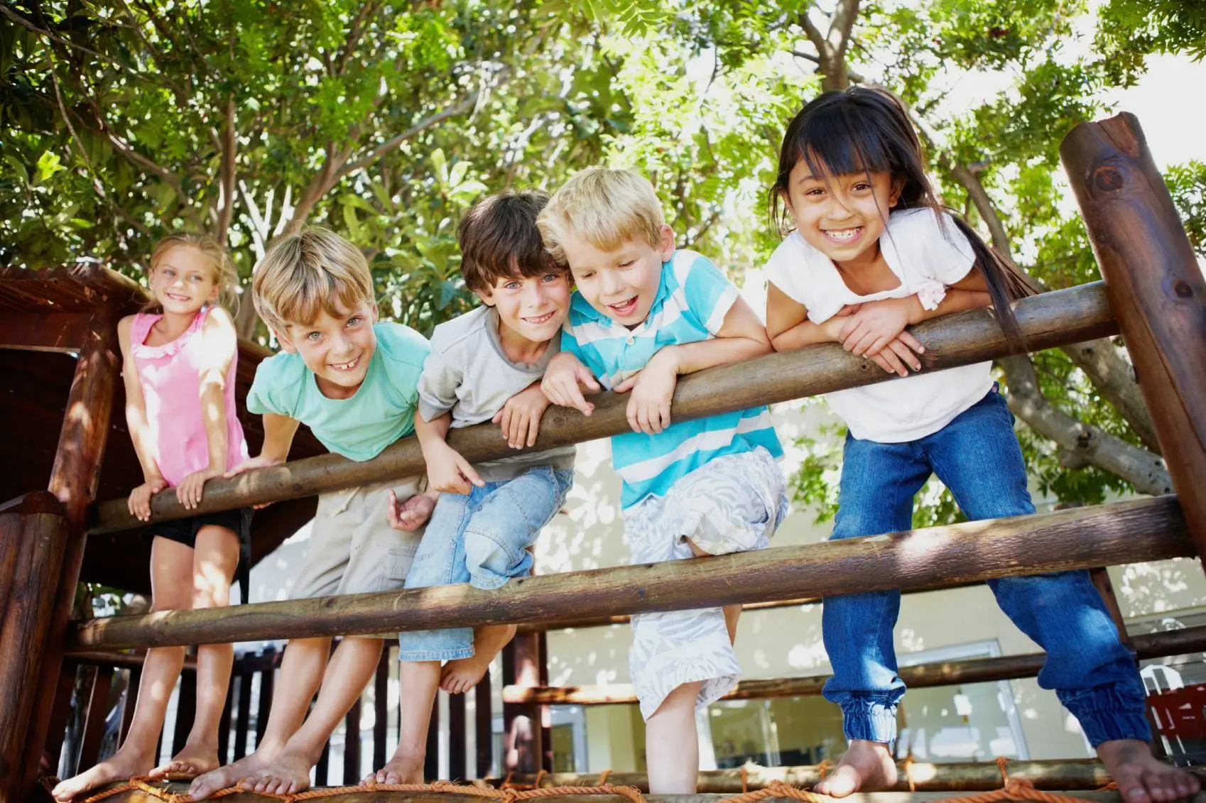 Five children standing on a wooden playground structure with trees in the background