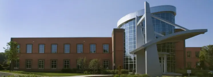A large brick building with a curved glass entrance and a white metal sculpture stands under a clear blue sky.