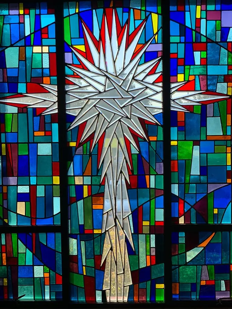 A stained glass window featuring a large white and red starburst design centered against a background of multicolored rectangular glass panels.