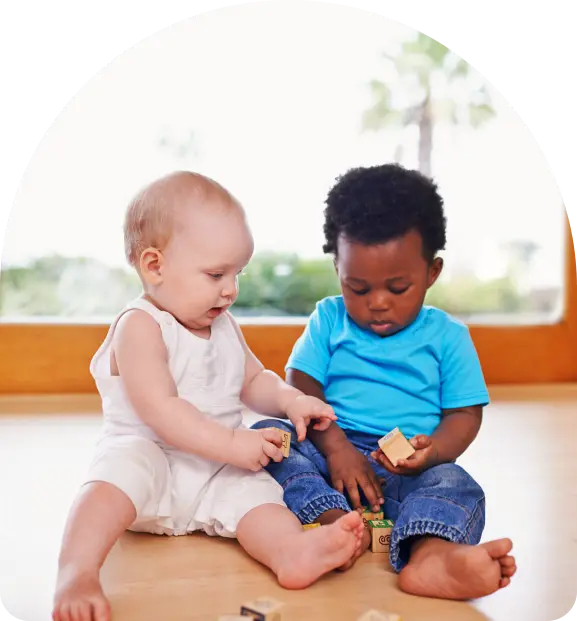 Two toddlers sitting on a wooden floor playing with small blocks.