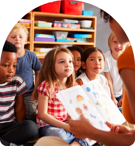 A group of preschool children sitting in a circle listening to an adult reading a book with colorful illustrations.