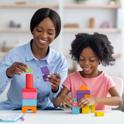 An adult and a child build with colorful building blocks at a table.