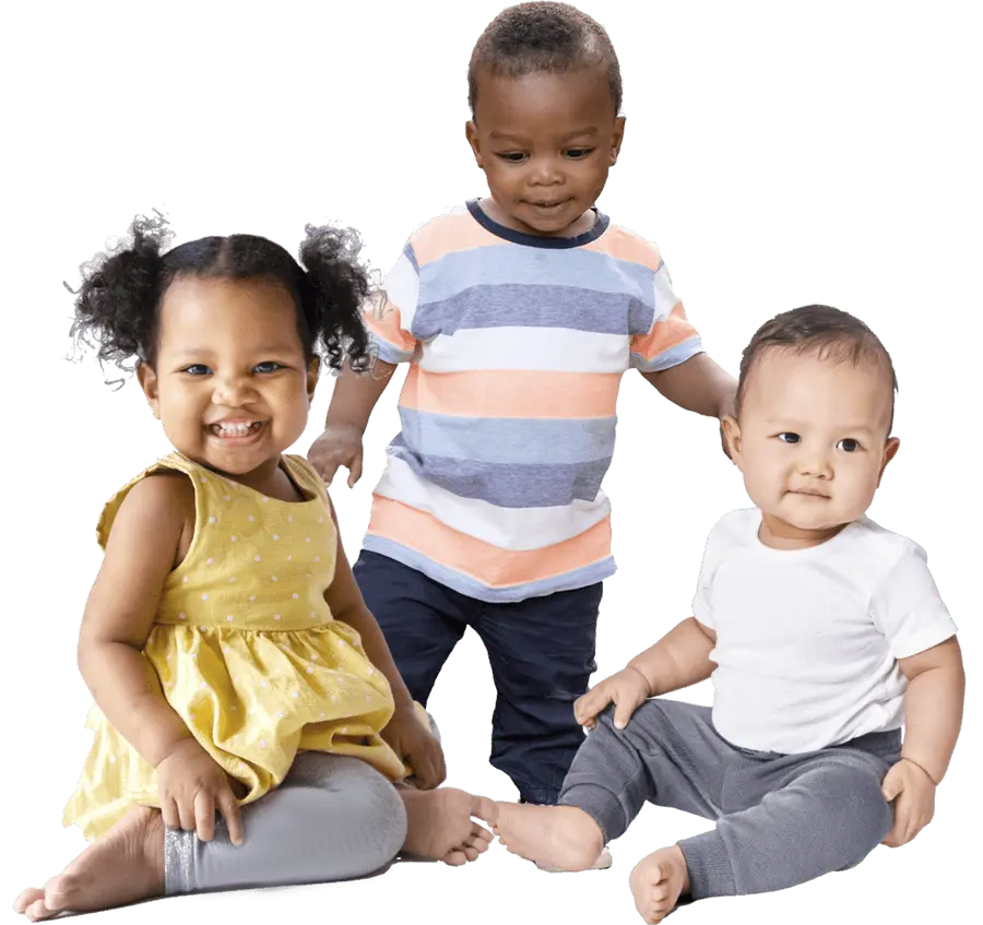 Three children sit and stand against a black background, with one girl in a yellow dress smiling, one boy in a striped shirt standing, and one baby in a white shirt sitting.