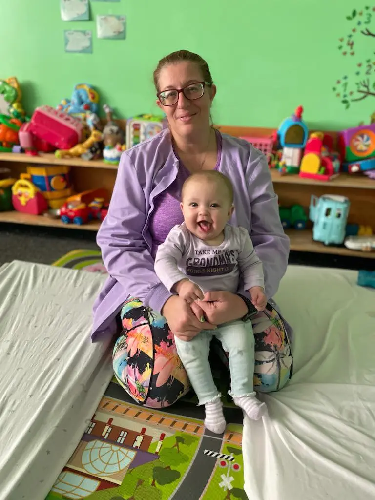 Adult holding an infant on a bed with toys in the background