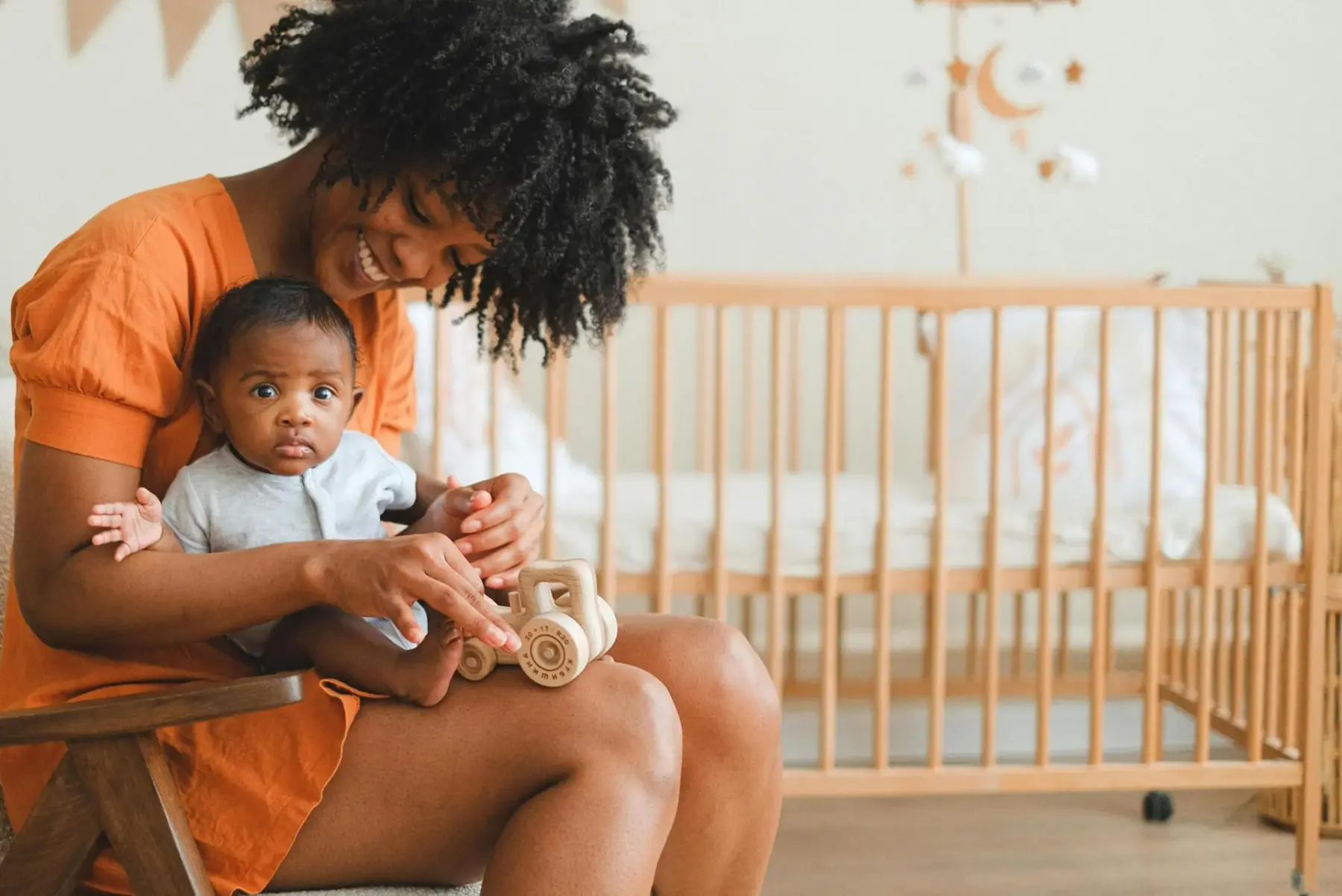 A woman holding an infant while playing with a wooden toy on her lap in a nursery setting.