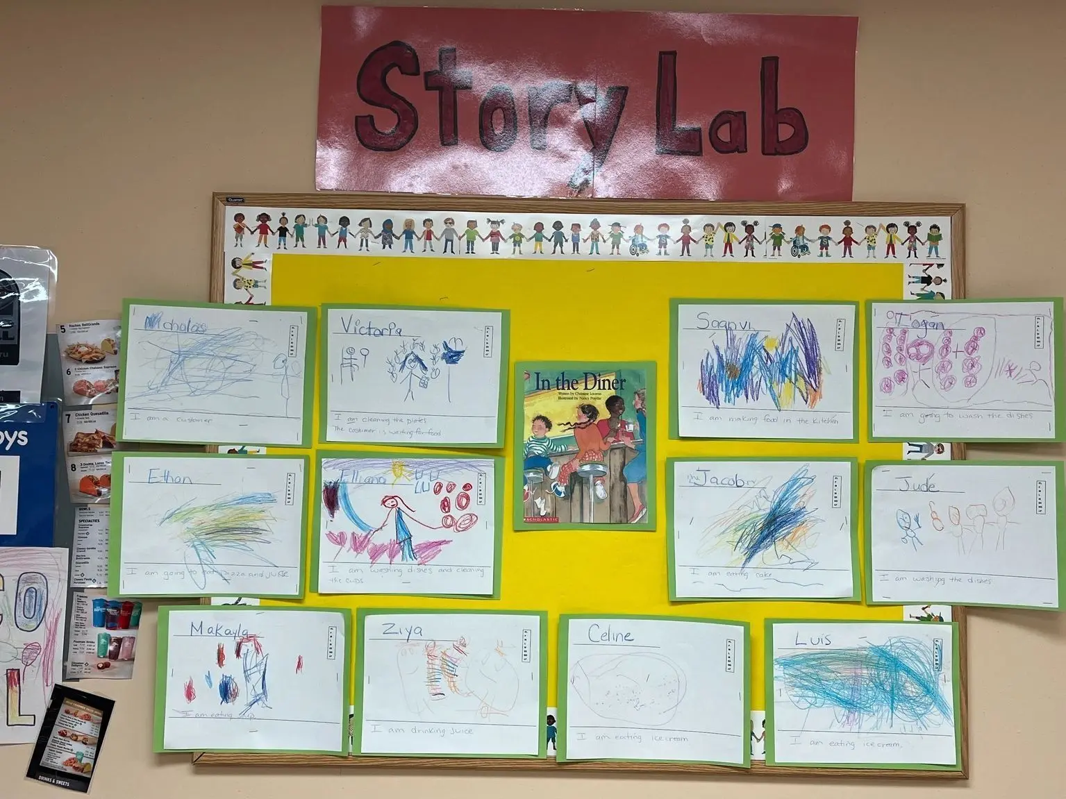 A yellow bulletin board displays a red 'Story Lab' sign, a children's book titled 'In the Diner,' and multiple framed drawings by children with their names and short sentences.